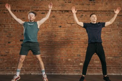 Two men performing jumping jacks in a gym setting, showcasing fitness and energy.
